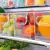 Organizadores multiuso transparentes com frutas como maçãs, laranjas e uvas, armazenados em uma geladeira.