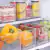 Conjunto de organizadores multiuso transparentes em uma geladeira, contendo frutas e bebidas.