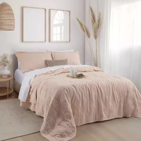 Habitación con cama vestida con cubrecama y funda de almohadón rosa de Jean Cartier.