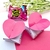 Dupla de lembrancinhas em forma de coração rosa, com um doce Sonho de Valsa ao fundo.