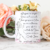 Caneca branca com mensagem bíblica e ilustração de mãos em oração, decorada com flores ao fundo.