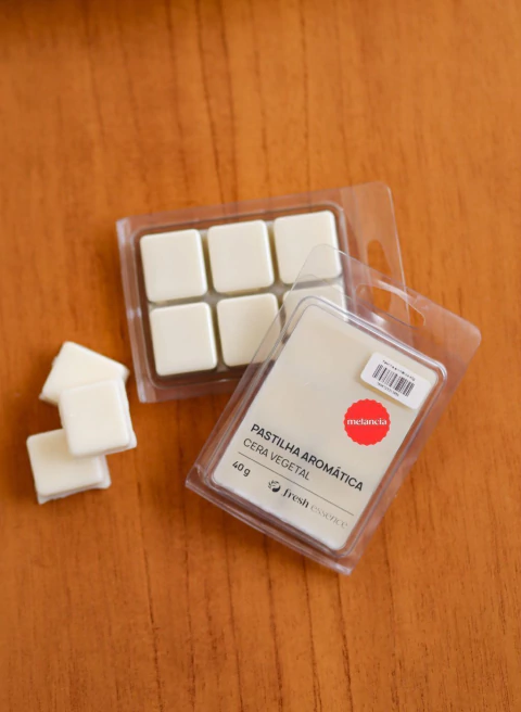 Pastilha aromática branca de cera vegetal com aroma de melancia em embalagem plástica transparente sobre superfície de madeira