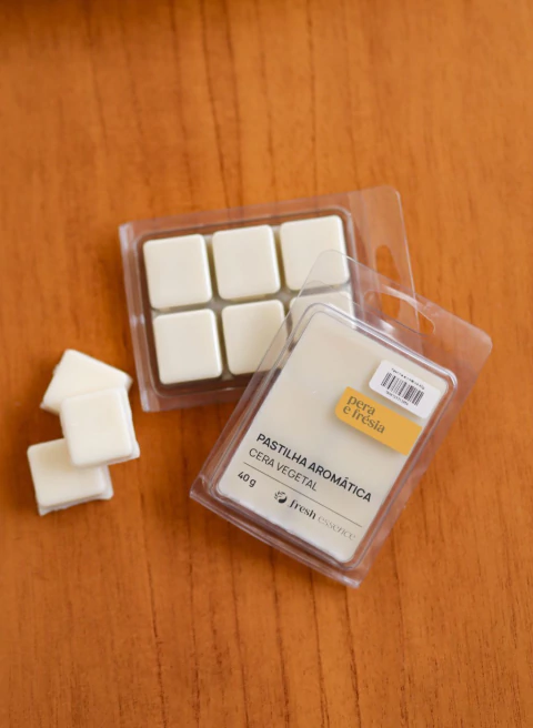 Pastilha aromática branca de cera vegetal sabor pera e frésia em embalagem transparente sobre superfície de madeira