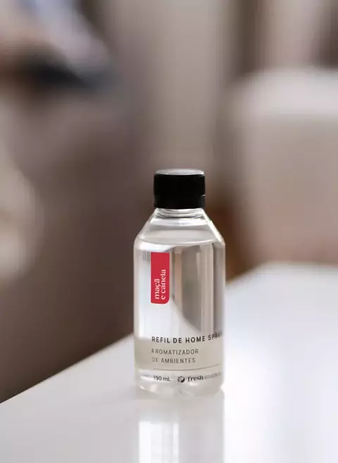 Refil de home spray aromatizador de ambientes com fragrância de maçã e canela em frasco transparente sobre mesa branca