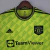 Camisa Manchester United Adidas 2022/23 Masculina em verde limão vibrante, com padrão geométrico de triângulos e listras. Gola redonda e ombros em azul marinho, escudo e logo Adidas em azul. Uma peça exclusiva celebrando a identidade gráfica do clube.