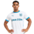 camisa titular oficial do Olympique de Marseille para a temporada 2024/2025, produzida pela PUMA. A camisa é predominantemente branca, com detalhes em azul e cinza nos painéis laterais. O escudo do clube aparece em uma versão especial dentro de um brasão,