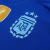 Camisa Reserva da Argentina 2024/25 Adidas. A camisa é predominantemente azul royal com detalhes em azul celeste e branco. Os arcos laterais são listrados em azul celeste e branco, e as três listras nas mangas e nuca são em azul celeste