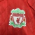 Camisa Retro Titular do Liverpool 2010-2012 em vermelho e branco. Camisa oficial usada durante a temporada turbulenta após a saída de Rafa Benítez e a chegada de Roy Hodgson. A equipe se recuperou com a volta de Kenny Dalglish e a contratação de Luis Suár