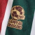 Camisa Titular do Fluminense Umbro 2024-2025. Camisa listrada em verde, branco e grená com gola V, mangas com listras e grafismo em Art Déco, escudo do Fluminense no lado esquerdo do peito, logo da Umbro no lado direito e patrocínio da Betano no centro.