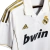 Camisa titular retrô Adidas do Real Madrid para a temporada 2011-12. A camisa branca e dourada apresenta o escudo do Real Madrid bordado no peito, o logotipo da Adidas nas mangas e ombros, o patrocínio da Bwin na frente da camisa e o nome e número do joga
