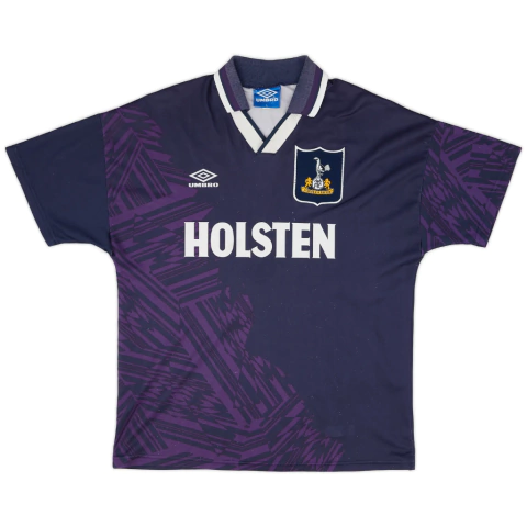 Camisa de futebol retrô do Tottenham Hotspur da temporada 1994-1995, modelo utilizado por Jürgen Klinsmann em sua estreia pelo clube. A camisa apresenta as cores azul marinho, roxo e branco, com o logo da Umbro e o escudo do Tottenham.