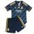 conjunto infantil reserva do Real Madrid Adidas 2023-2024. A camisa é azul marinho com um design de ondas em tom mais claro. A gola é redonda e há detalhes em azul marinho nas laterais e na barra. As três listras nos ombros são amarelas, brancas e roxas.