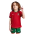 Conjunto Infantil Titular da Seleção Portuguesa Nike 2024-2025. Camisa vermelha com gola preta e verde, calção verde e escudo da FPF. Inspirada na bandeira portuguesa. Vista frontal de um menino vestindo o conjunto completo, em pose de comemoração.