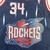 Regata away Houston Rockets da temporada 1996-1997, modelo swingman, da marca Mitchell & Ness. A imagem mostra a parte frontal da regata com o número e nome de Hakeem Olajuwon, além dos logotipos da equipe e da NBA.