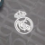 terceira camisa do Real Madrid para a temporada 2024/2025. A camisa é predominantemente cinza carvão com a sigla "RMCF" aplicada em jacquard ao longo de todo o corpo. A gola polo possui frisos em rosa e cinza escuro, assim como os punhos. O escudo do Real
