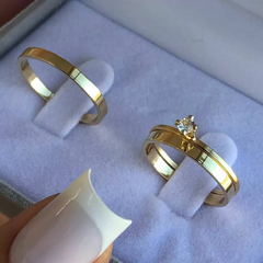 Par de alianças banhadas a ouro 18k, com uma aliança destacando um pequeno cristal, apresentadas em uma caixa de veludo.