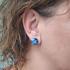 Brinco botão de sodalita azul em orelha feminina, destacando a textura e cor da pedra.