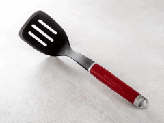 Espátula perfurada vermelha com alça para pendurar da KitchenAid, ideal para cozinhar e servir alimentos.