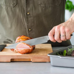 Um chef usando uma faca de cozinha KitchenAid para cortar carne em uma tábua de madeira.
