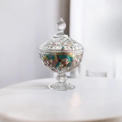 Bomboniere decorativa de vidro com pé, cheia de doces coloridos, sobre uma mesa.