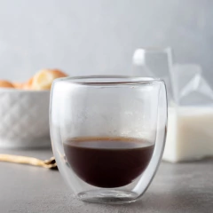 um copo de parede de vidro duplo com café em uma mesa com alimentos