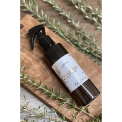 Frasco âmbar com home spray de ambientes e água de tecidos aroma alecrim da marca Mels Brushes sobre apoio em madeira e ladeado por ramos de alecrim. 