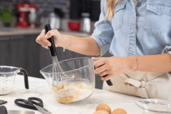 Uma pessoa misturando ingredientes em uma jarra medidora KitchenAid de 2 litros, com uma batedeira, em uma bancada de cozinha.