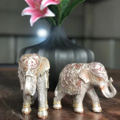 Estatuetas de elefantes em prata decorativa, uma ao lado da outra, com detalhes ornamentais, sobre uma mesa de madeira.