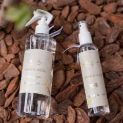 Imagem de dois frascos de spray aromatizante Vanilla Musk da Mels Brushes, um de 500 ml e outro de 200 ml, sobre uma superfície de cascas de cacau.