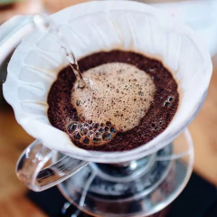 Filtro de papel Hario V60 em uso, com água sendo vertida sobre o café moído, formando uma camada de espuma.