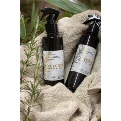 Dois frascos âmbar com home spray de ambientes e água de tecidos aroma alecrim da marca Mels Brushes sobre toalhas acinzentadas e ramos de alecrim.