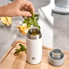 mulher colocando planta para chá dentro de uma garrafa térmica 