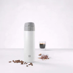 garrafa térmica cinza e branca com trava e gravação da marca pequena na parte de baixo da garrafa ao lado de grãos café