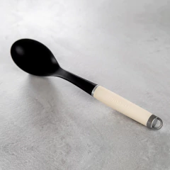 Colher de servir nylon com alça creme da KitchenAid sobre uma superfície de pedra clara.