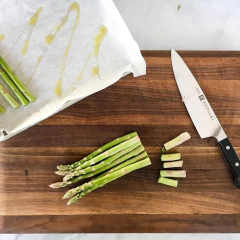faca chef com cabo sintético preto e lâmina gravada com a marca do lado de um legumes