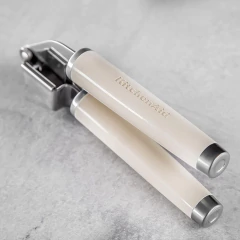 Amassador de alho KitchenAid em creme, com cabo de inox, sobre superfície de pedra.