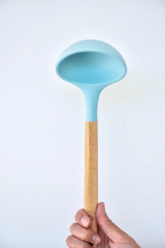 mulher segurando uma concha de silicone azul claro com cabo de madeira