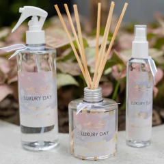 Conjunto de difusores de aromas da linha Luxury Day, incluindo um frasco com palitos, um spray e outro frasco, todos com rótulos elegantes.
