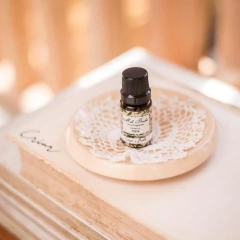 Frasco de essência 10ml de cereja e avelã da Mels Brushes, colocado sobre um suporte de madeira decorativo com uma rendinha.