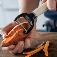 Um descascador de legumes e frutas da KitchenAid sendo usado para descascar uma batata-doce.