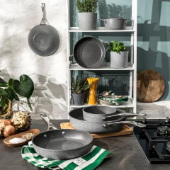 frigideiras ballarini posicionadas em uma estante e uma mesa junto de tábuas de madeira, vasos de plantas, panos e alimentos