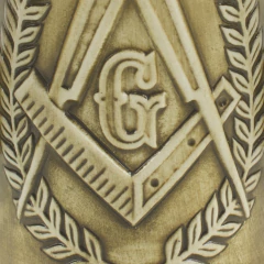 Detalhe de um caneco de cerâmica com símbolo da maçonaria, apresentando esquadros e compasso, decorado com folhas.