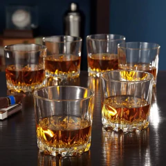 Conjunto de copos baixos de whisky transparentes com bebida âmbar em uma mesa escura.