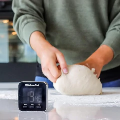 Temporizador digital KitchenAid mostrando 19 minutos e 48 segundos, enquanto uma pessoa amassa massa em uma superfície de trabalho.