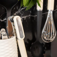 Batedor de ovos em creme KitchenAid, posicionado ao lado de utensílios de cozinha em um ambiente moderno.