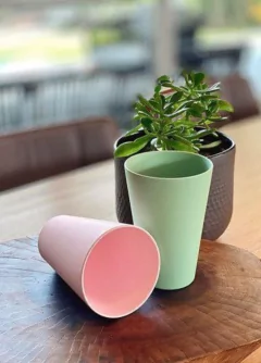 copo de fibra de bambu redondo com a base menor que a boca rosa claro ao lado de um copo azul turquesa