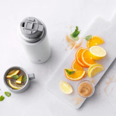 garrafa térmica branca / cinza com a marca gravada no inferior da garrafa térmica ao lado de uma laranja cortada