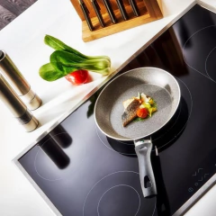 Frigideira antiaderente em alumínio Bologna Granitium de 24cm com peixe e legumes na superfície de uma cozinha moderna.