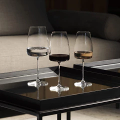 Três taças de cristal para água, com diferentes bebidas, sobre uma mesa de centro moderna.