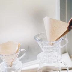 Suporte acrílico para filtro de café Hario V60-03 com filtro de papel sendo colocado em um dos coadores.